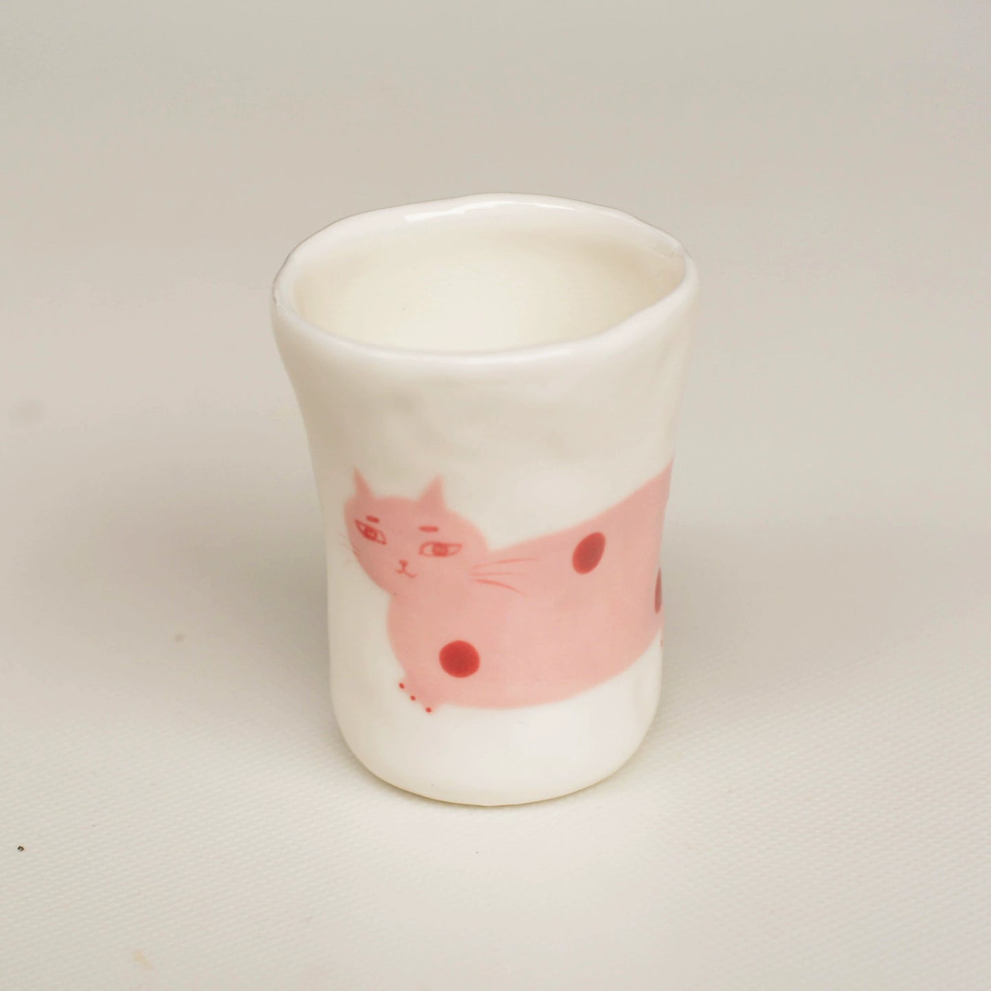 White ceramic cup with a pink cat design on a light gray background